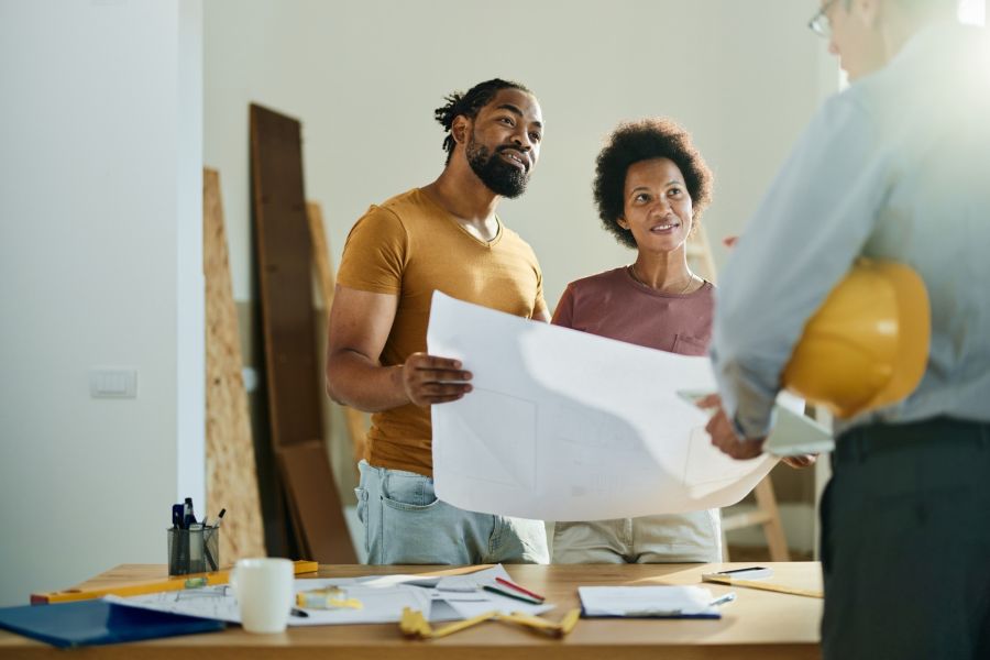 Couple reviewing home renovation plans with a contractor in a room under renovation