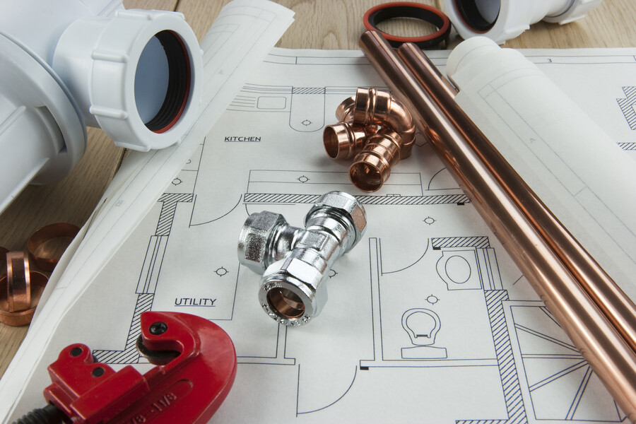 Copper pipes and plumbing fittings on a house blueprint with kitchen and utility room layout
